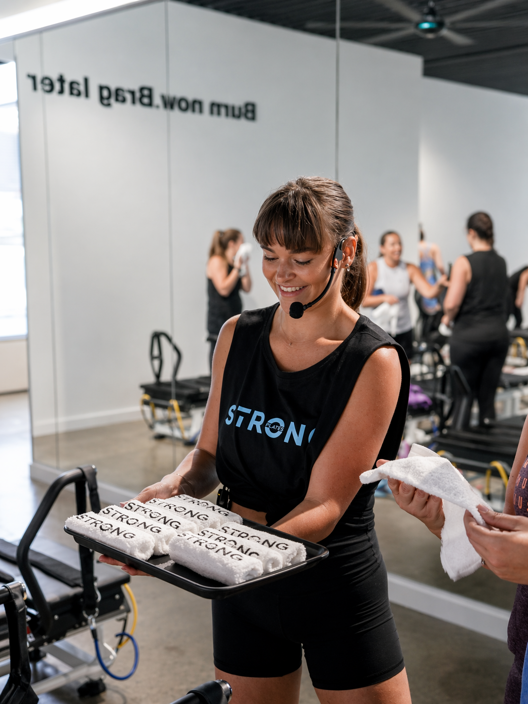 Elle in a Strong studio holding a tray with towels and ‘STRONG’ tank top.