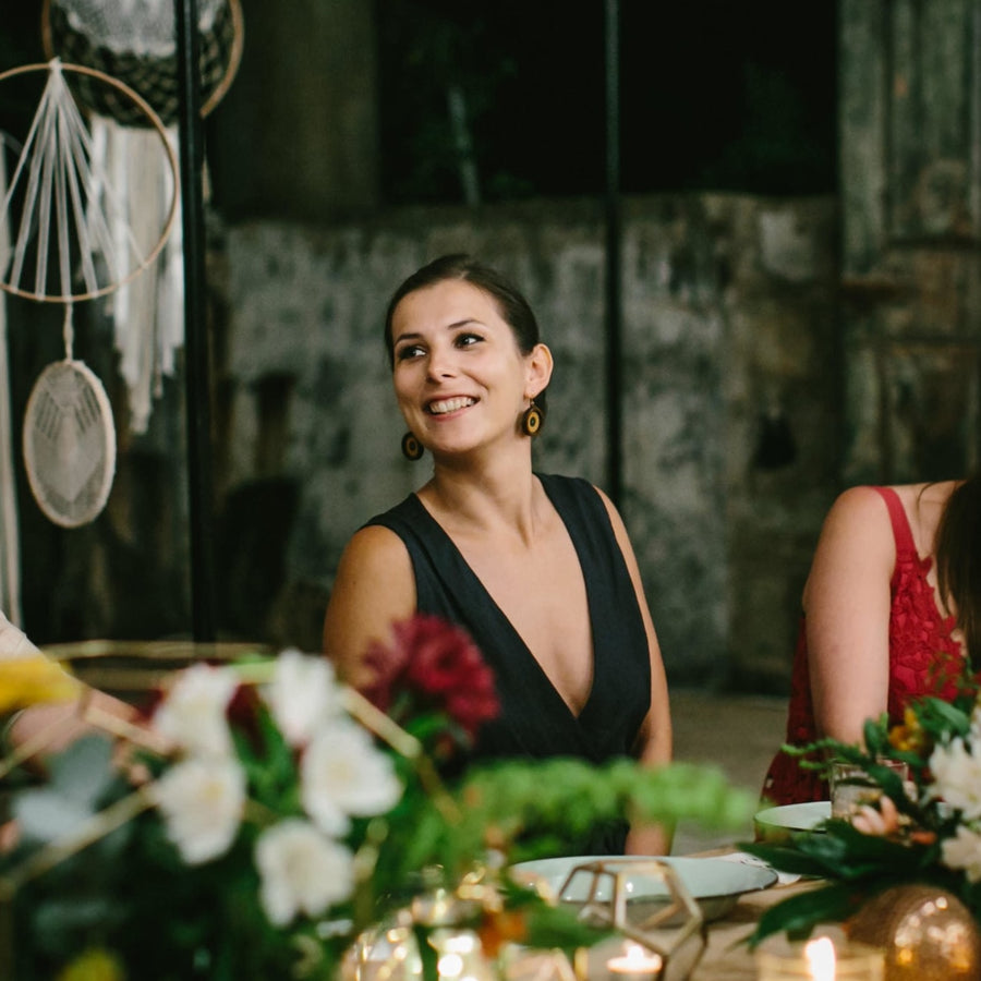 Diana Coffey in a navy playsuit sitting at a table with floral decorations and a stone wall background.