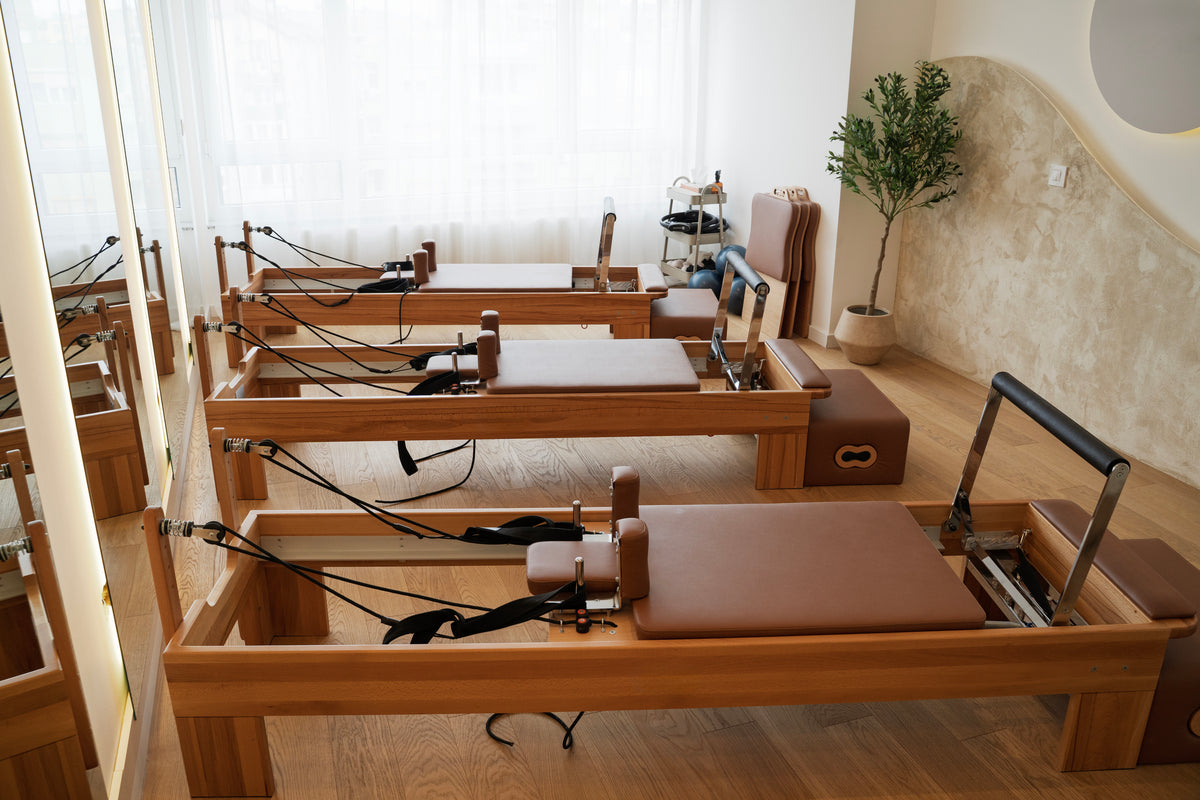 Pilates reformers in a studio with wooden floors and large windows.