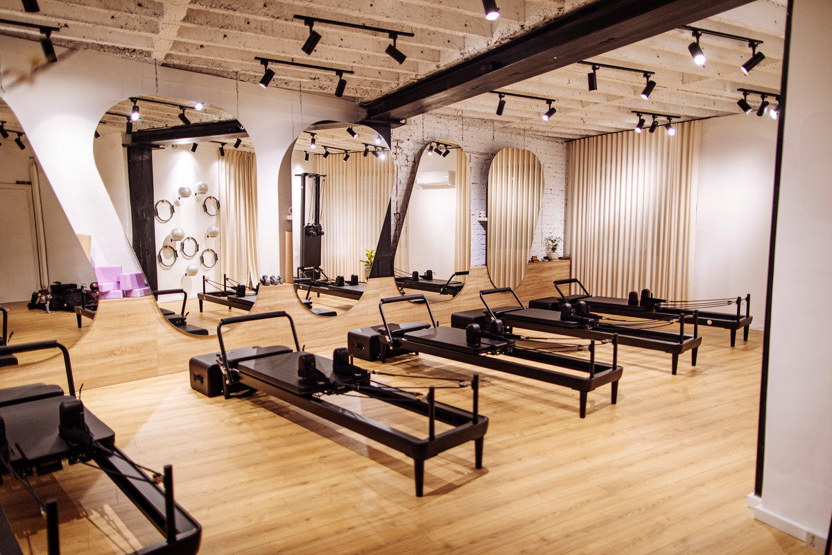 A warm, editorial wide shot of a reformer studio floor, lit from the side.